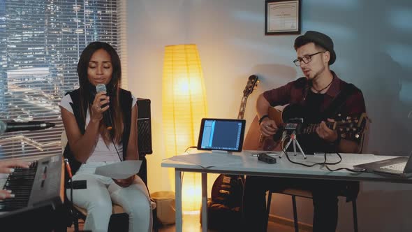 Band Rehearsing in Home Studio: Young Man Playing Guitar and Mixed-race Girl Singing Into Microphone