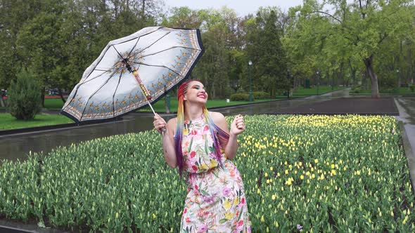 Girl with African Braids and Makeup in Spring Dress is Dancing in the Rain with Umbrella in Yellow