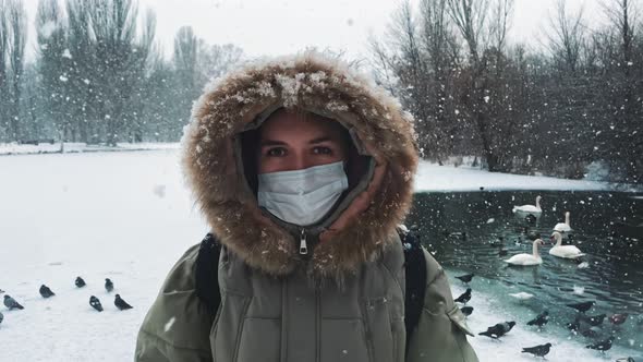 Portrait of Woman in Walking in a Park in Winter Under Snowfall in a Protective Mask to Protect