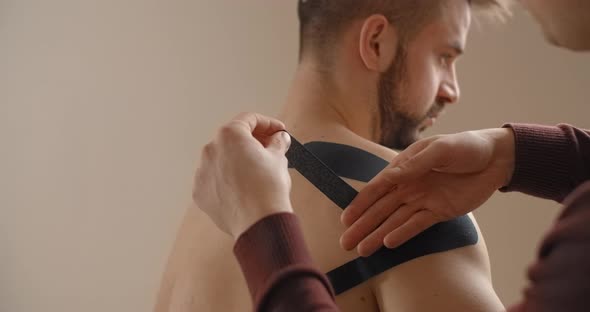 Kinesiologist Sticks Tapes to the Shoulder of Man Recovery of an Athlete After Injury Kinesiotherapy