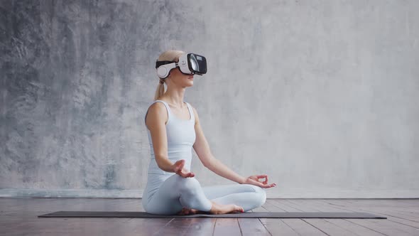 Young and sporty girl in sportswear is doing exercises at home using virtual reality helmet.