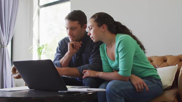 A young caucasian couple talking and paying their bills using a laptop