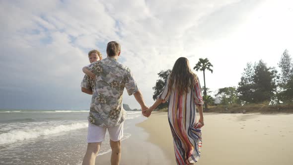 4K Caucasian family parent with little baby son holding hands and walking together on tropical beach