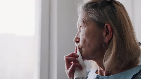 Elderly Woman Wiping Her Mouth with Napkin While Looking Through the Window