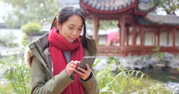 Woman wearing winter jacket and use of mobile phone in china garden