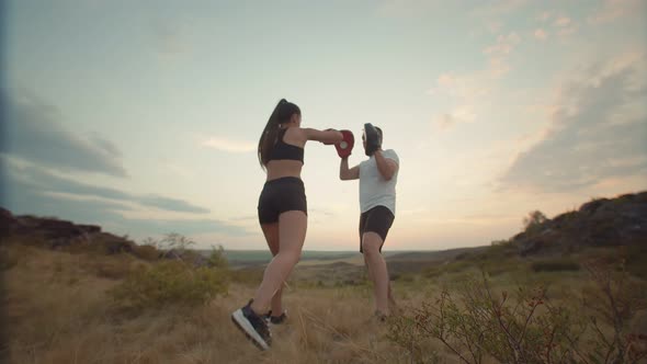 Female Boxer in Black Suit Trains with Trainer at Sunset in Field