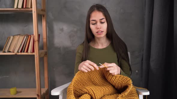 a Young Girl Knits a Warm Sweater in Front of a Laptop