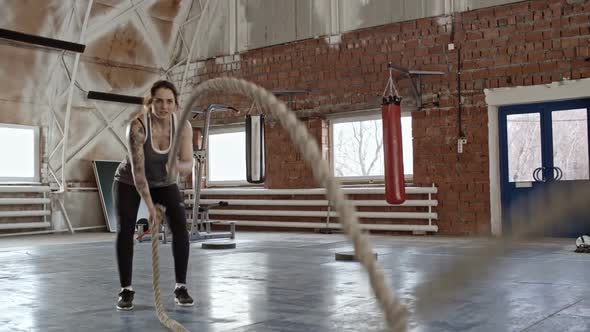Tattooed Sportswoman Doing Battle Rope Arm Exercise