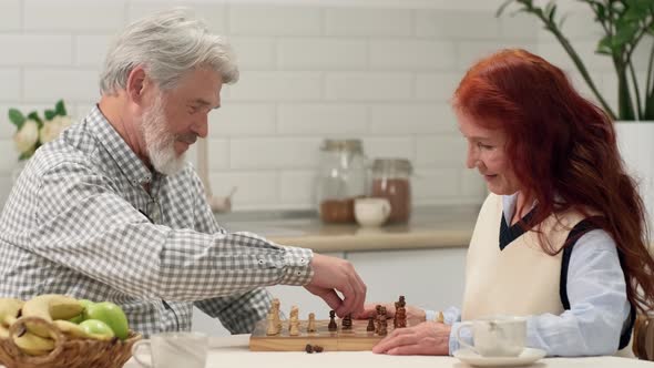 Happy Senior Couple 6070 Years Old Playing Chess at Home Sitting at the Table in the Kitchen