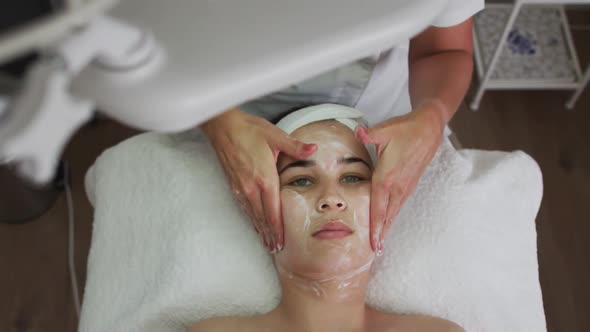 Caucasian woman lying back while beautician gives her a facial