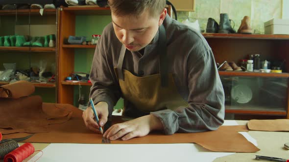 Slowmotion Video. A Young Tanner Makes Marks with a Pencil and Ruler on a Piece of Genuine Leather