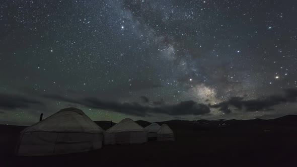 Milky Way Is Moving Across Starry Sky with Clouds Over Yurt Camp