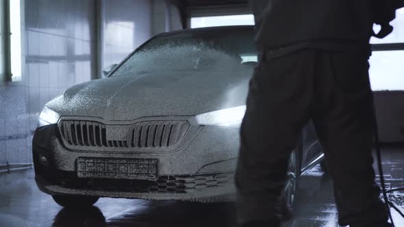 Worker Spraying Car with Pressure Washer in Auto Care Shop. Employee Washing Automobile with Special