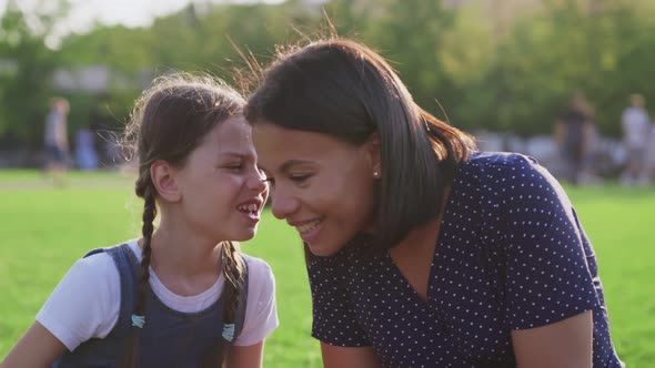 Closeup of Preteen Girl Whispering Secret to Surprised Mother at Park