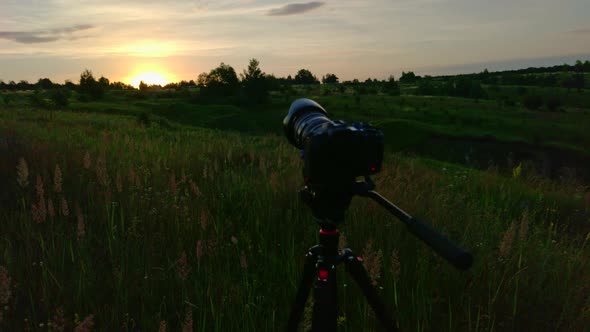 Camera on Tripod Shooting Sunrise in Summer Meadow