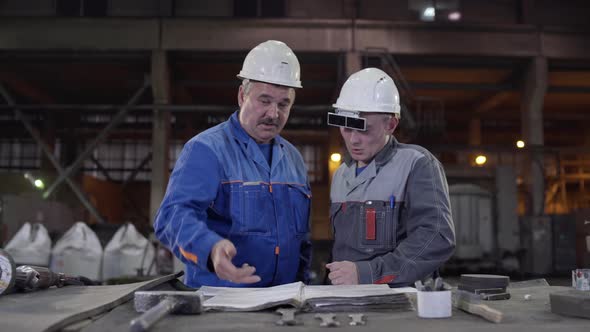 Two Workers at Heavy Industry Factory Have Conversation While Looking at Blueprint. Engineers