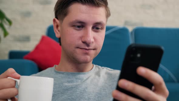 Man Write a Message Using a Mobile Phone While Is Drinking a Cup of Tea