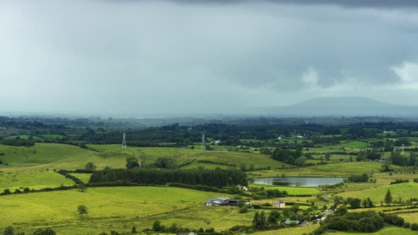 Time lapse of rural farming landscape with grass fields, lake and hills during a passing storm rainy alt