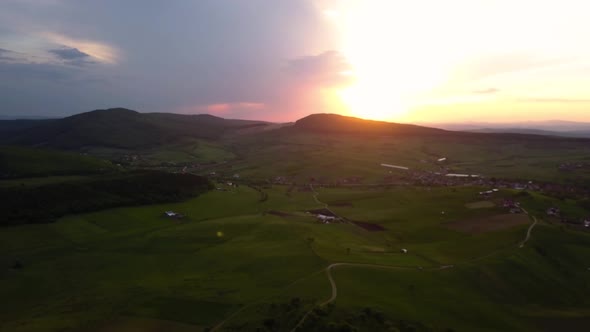 Aerial pan of a sunset over wide fields and green meadows near a town, Transylvania, Romania