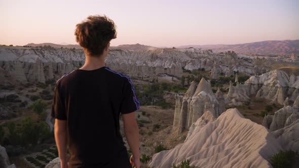 Young man stands on mountain top overlooking view and sunset