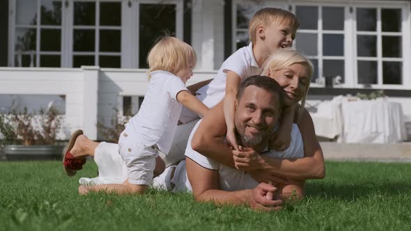 Happy Family with Children Rejoice Lying on the Grass. Mom and Two Sons Lie on Top of Dad