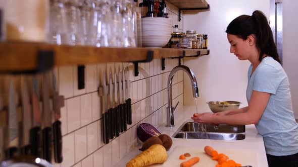 Woman washing carrot in the kitchen sink