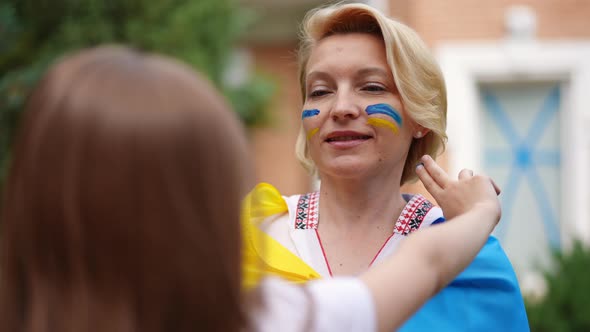Portrait of Proud Mother Smiling As Daughter Drawing Ukrainian Flag Colors on Cheeks Leaving