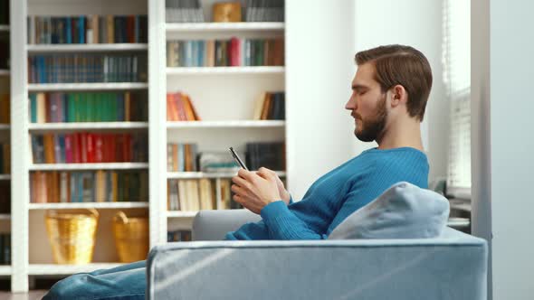 Serious male typing on smartphone on sofa