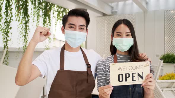 Business owner attractive young Asian couple in apron hanging we're open sign