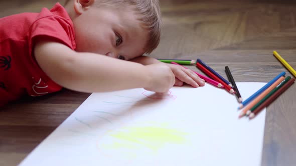 Little Baby Boy Lying on the Floor and Drawing Summer Picture with Colorful Pencils