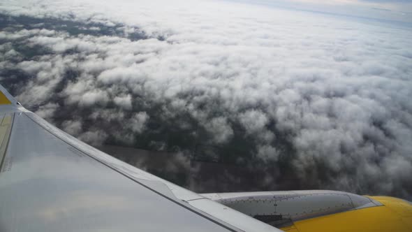 POV airplane passenger window: white blanket and billowing clouds below with view of aircraft wing a