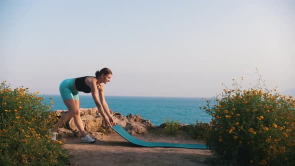 A Woman in Sportswear Spreads a Yoga Mat on a Hill By the Sea