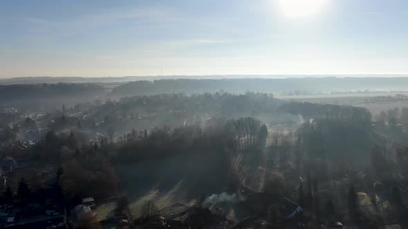 Aerial View of Forest and Farmland During Foggy and Cold Winter Morning with Blue Sky Facing the Sun