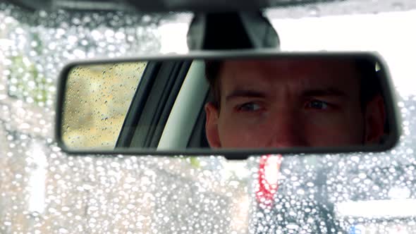 Young Handsome Man Sits in Car - Detail of Face in Rear-view Mirror