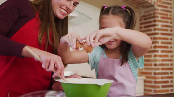 Caucasian mother and daughter wearing aprons baking together in the kitchen at home