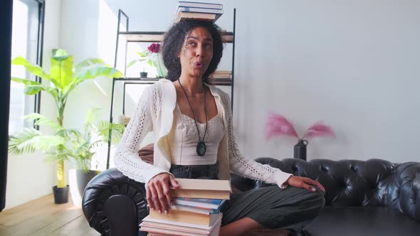 Young Attractive Ethnic African American Woman with Books on Head Sits on Sofa