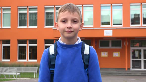 A Young Boy Smiles at the Camera - an Elementary School in the Background