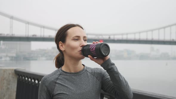 Thirsty Female runner drinking water from bottle after outdoor workouts. Running concept