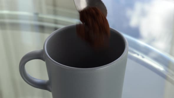 Two spoons of coffee to preparing a morning drink into grey mug, close-up view.