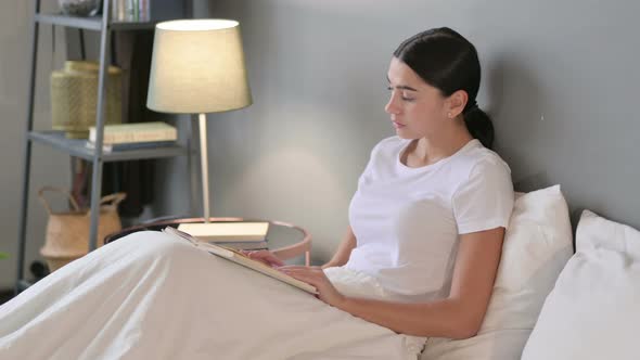 Focused Young Latin Woman Reading Book in Bed 