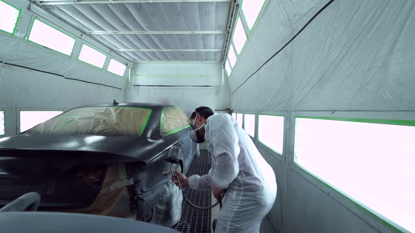 Car body painter spraying car in paint booth