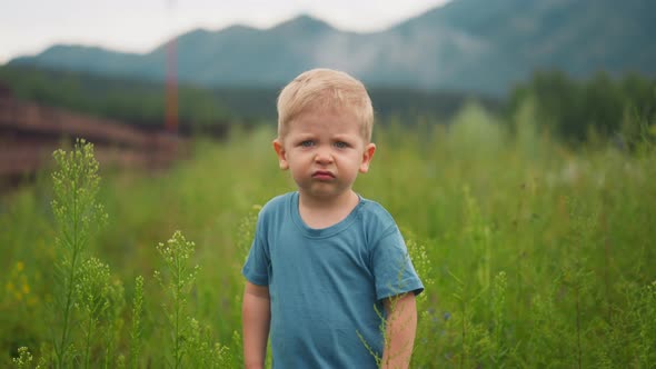 Unhappy Little Boy Grimaces Walking Along Meadow Grass