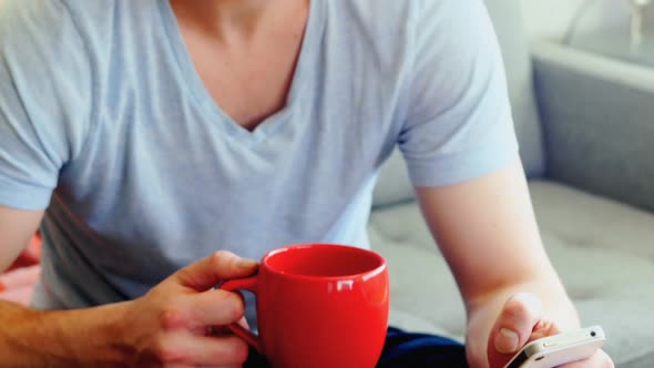 Man using mobile phone while having coffee in living room 4k