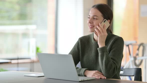 Young Woman with Laptop Talking on Smartphone 