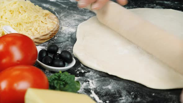 Female hands are forming dough on floured black table and rolling out with rolling pin