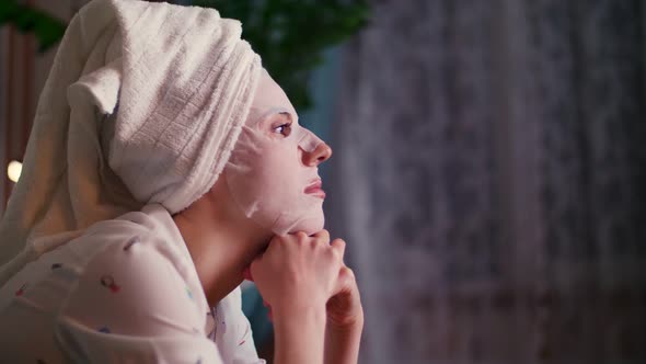Profile Portrait, a Woman in a Cosmetic Fabric Mask and with a White Towel on Her Head, Under Light