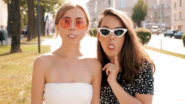 Portrait of two young beautiful smiling hipster girls in trendy summer clothes