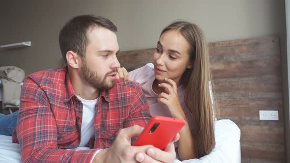 Young Family Watches Online News on Smartphone While Lying a Bed in Their Bedroom