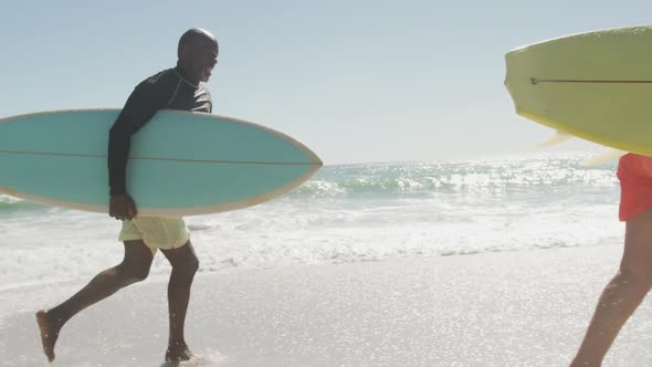 Smiling senior african american couple running with surfboards on sunny beach