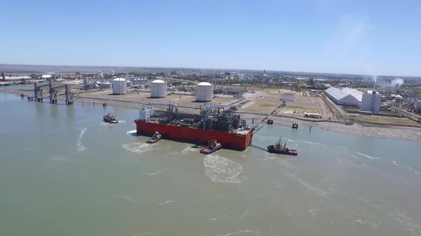 Aerial view of cargo ship arriving at the port with the help of tugs.